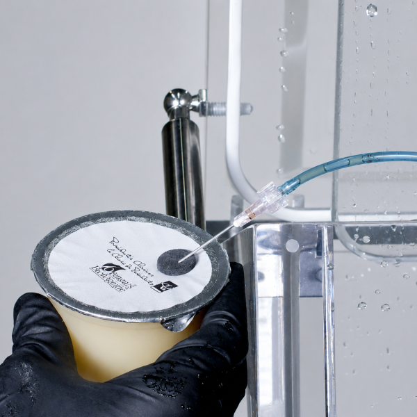 VAC Attachment needle injecting air through a septum patch on a vacuum-sealed cup during a bubble leak test in a FlexPak vacuum chamber