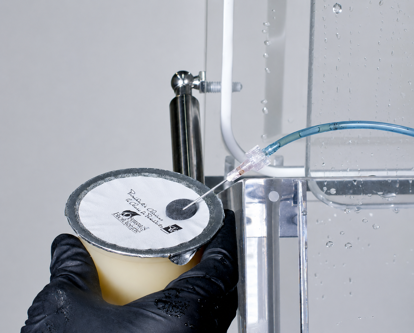 VAC Attachment needle injecting air through a septum patch on a vacuum-sealed cup during a bubble leak test in a FlexPak vacuum chamber